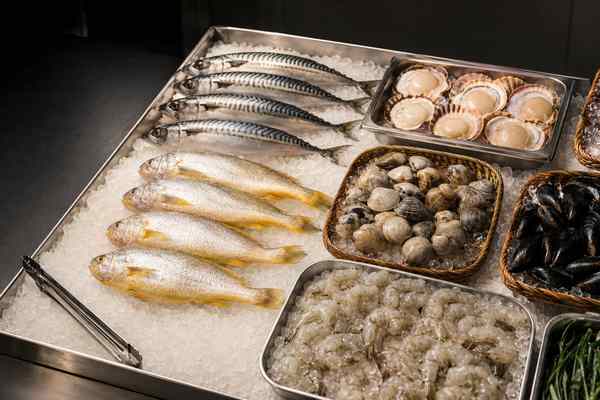 Whole mackerel and yellow croaker, scallops, clams, mussels, and peeled shrimp on crushed ice in metal trays and baskets, with tongs alongside.