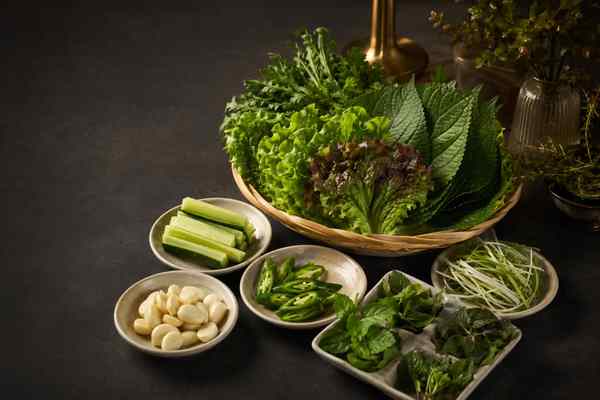 Bamboo basket of leaf lettuce, perilla, and crown daisy, with small dishes of cucumber, peeled garlic, sliced green chili, herbs, and shredded scallion.